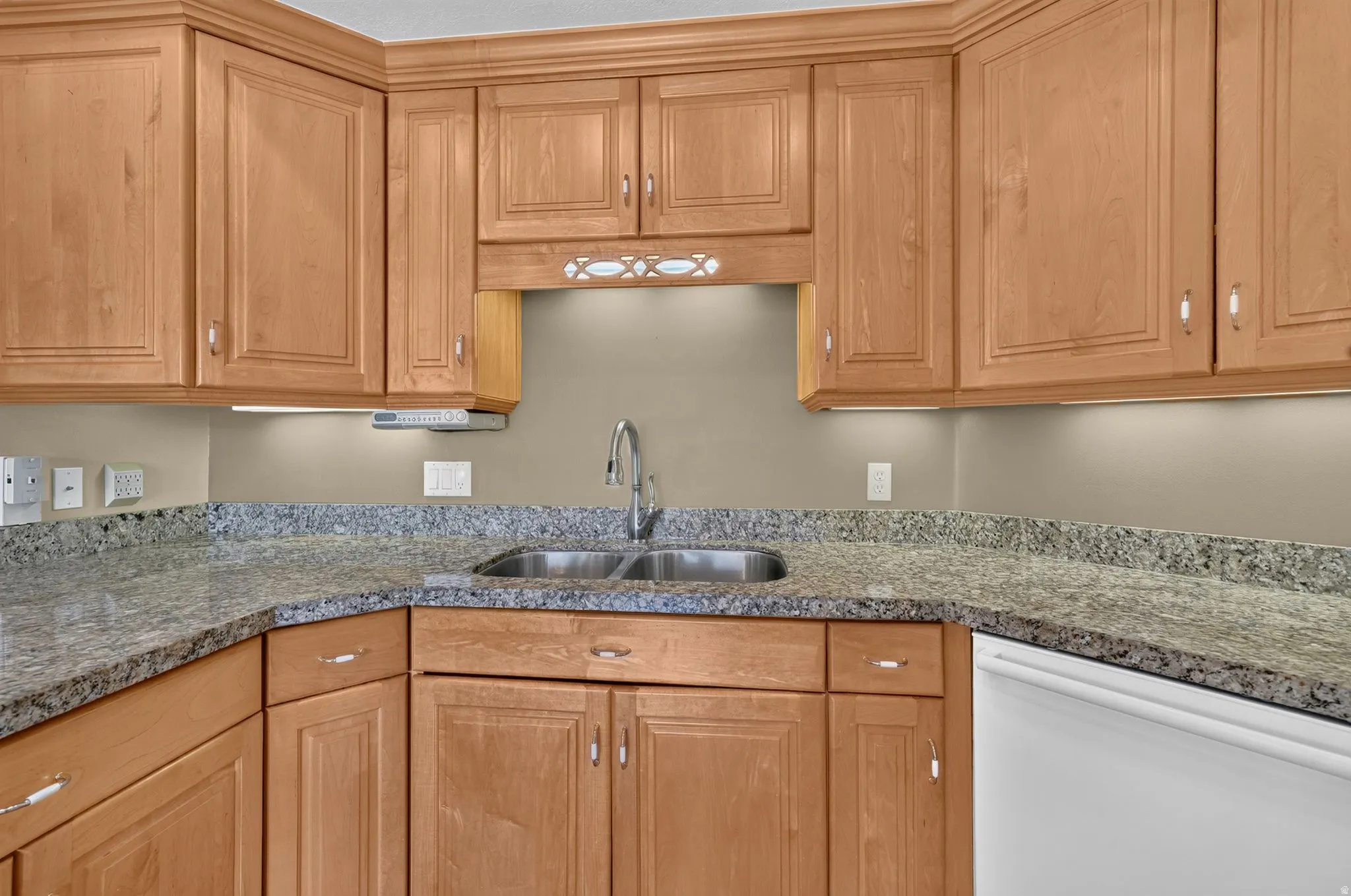 Kitchen featuring light wood cabinetry with crown molding, stone countertops, a double basin sink with a gooseneck faucet, and under-cabinet lighting