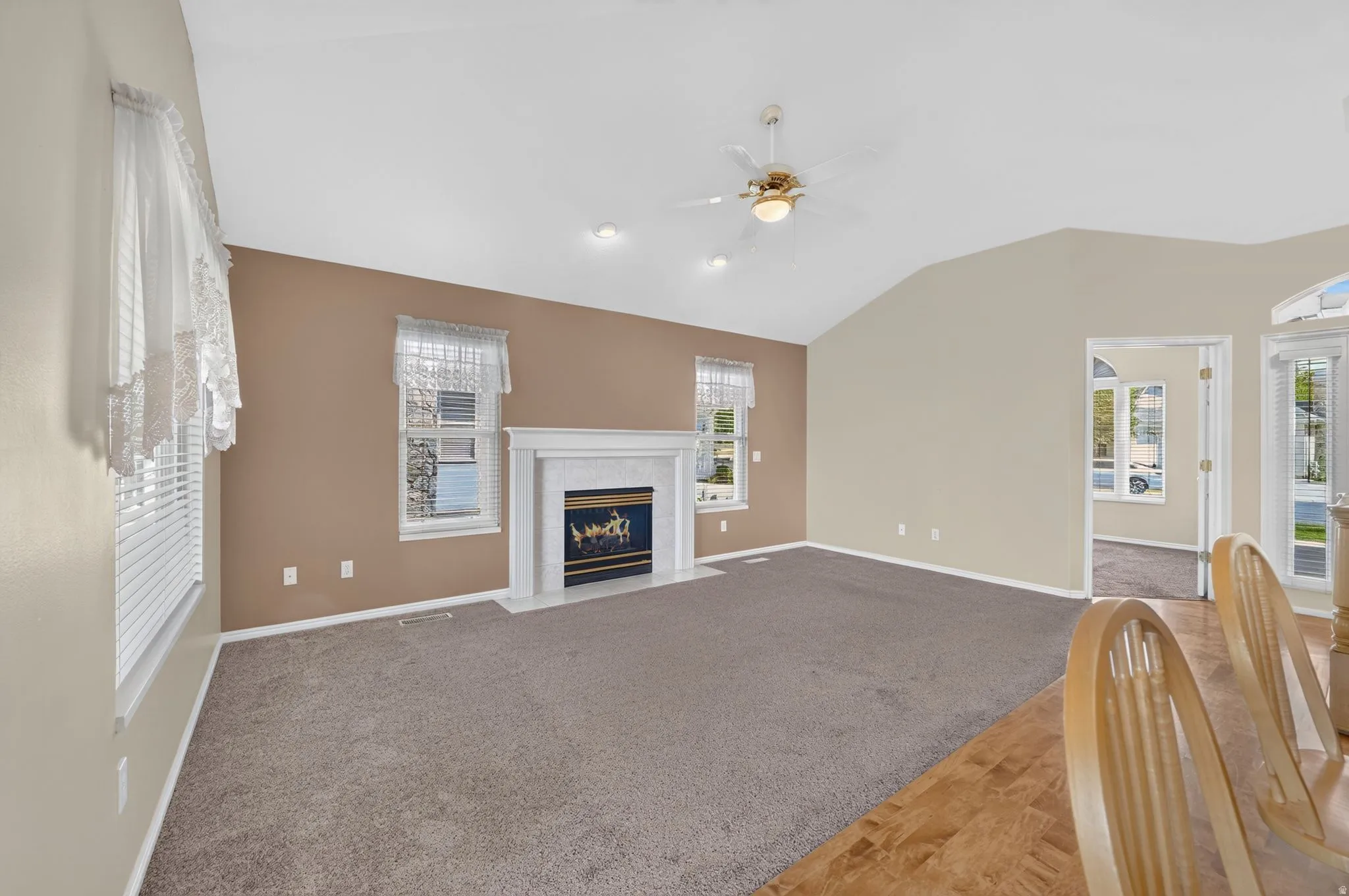 Carpeted living area featuring a central fireplace with a white mantel, vaulted ceilings, and a ceiling fan