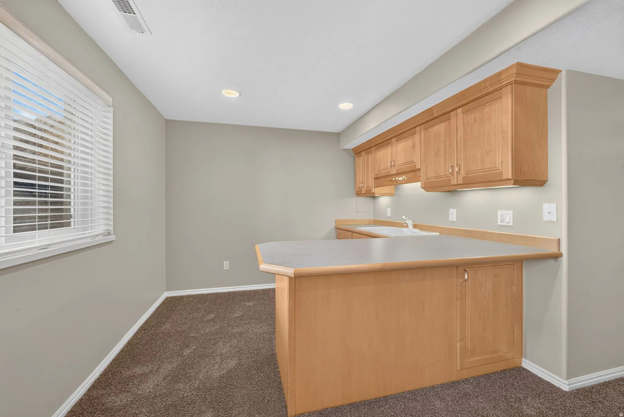 Kitchenette featuring light wood cabinetry, a built-in sink, and a light-toned countertop