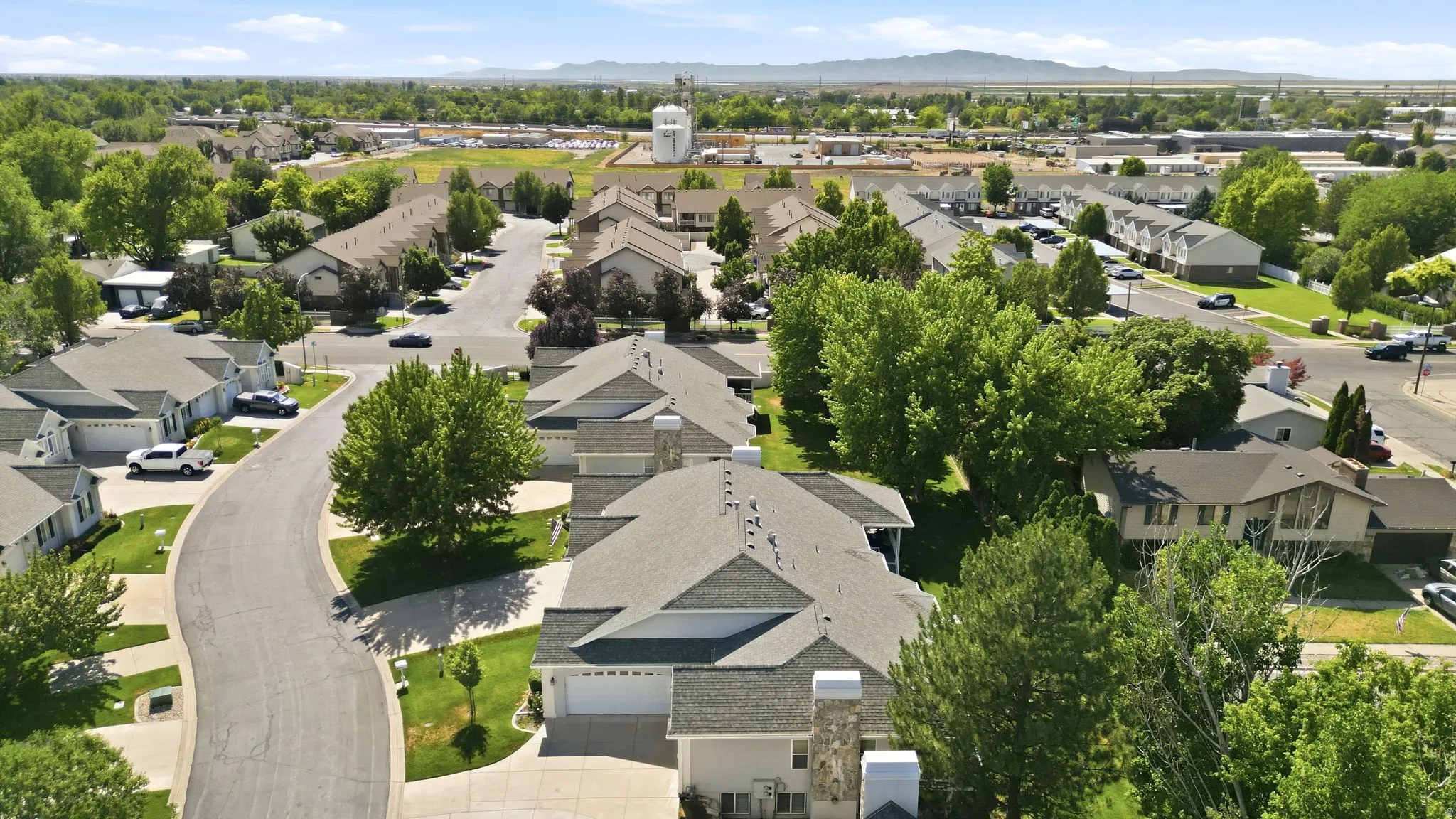 Residential street featuring detached homes with attached garages, shingled roofs, and mature trees throughout