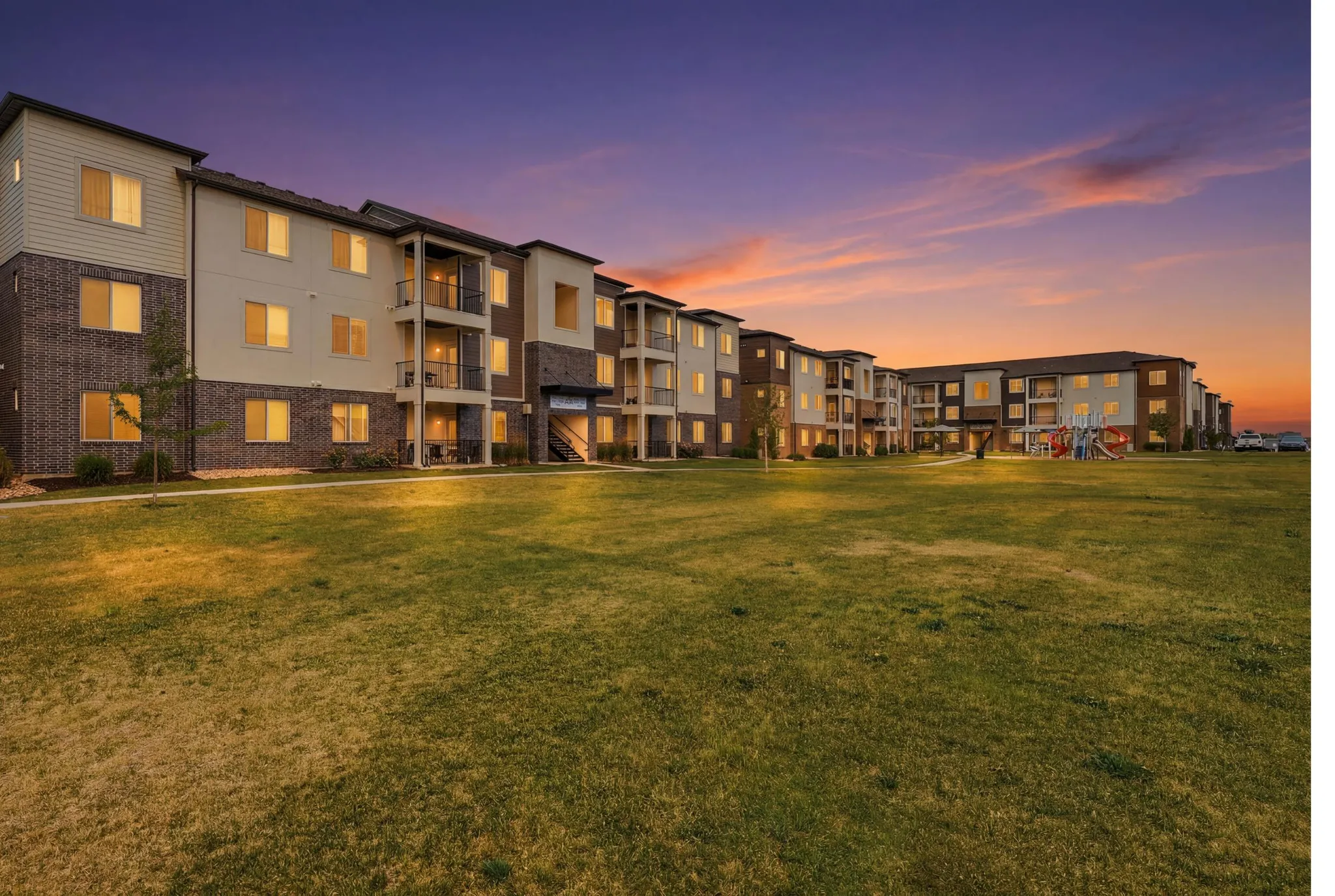 Expansive green space fronting a multi-story residential building with private balconies and a children's play structure