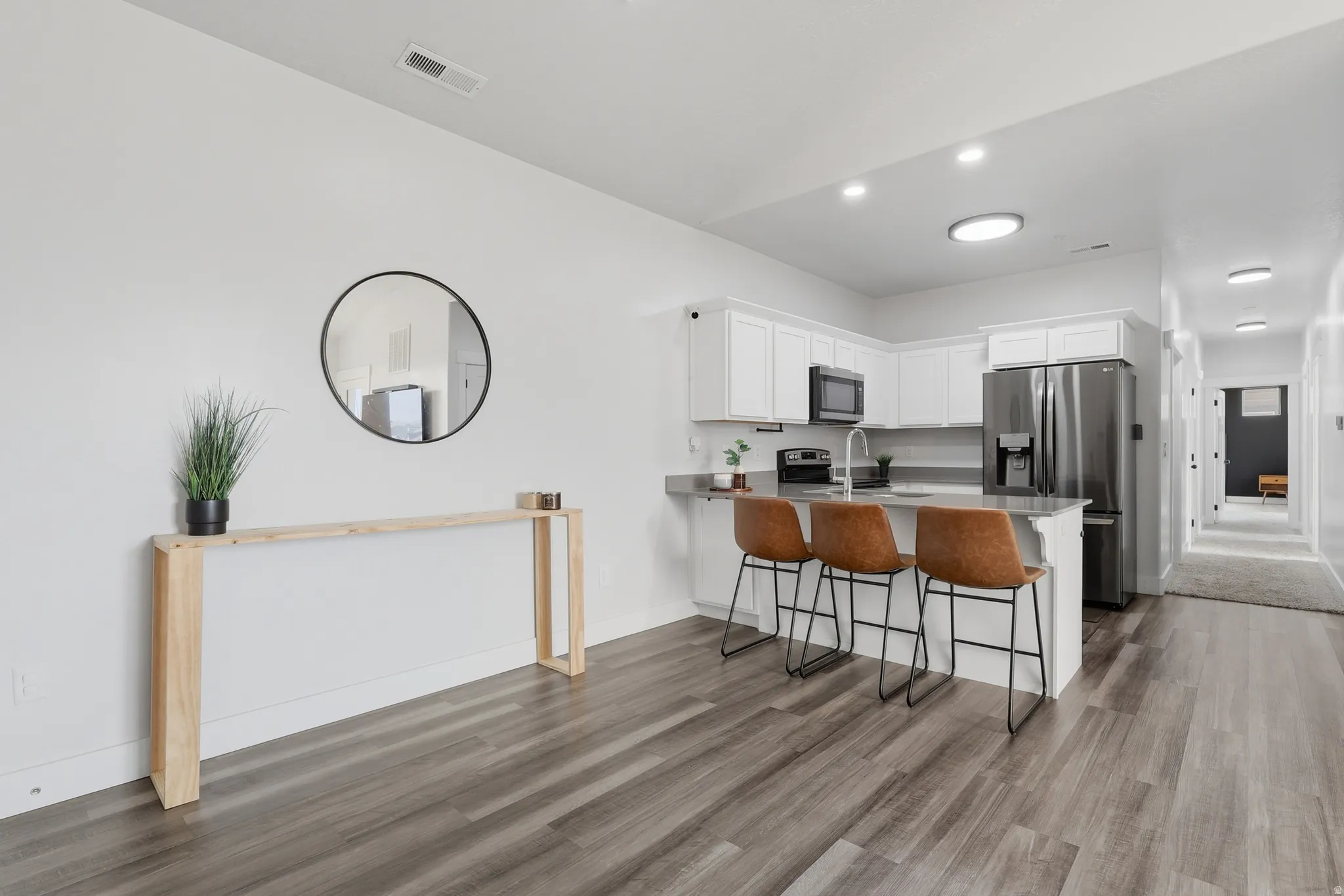 Open-concept kitchen featuring white cabinetry, gray countertops, a stainless steel refrigerator, and a kitchen island with seating