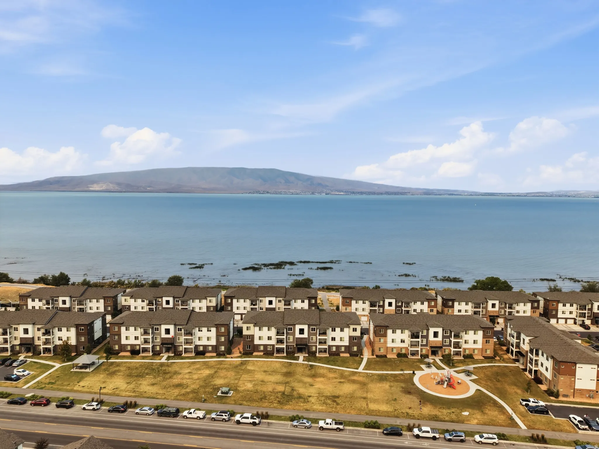 Waterfront apartment complex featuring multi-story buildings with balconies, a central playground, and paved parking areas