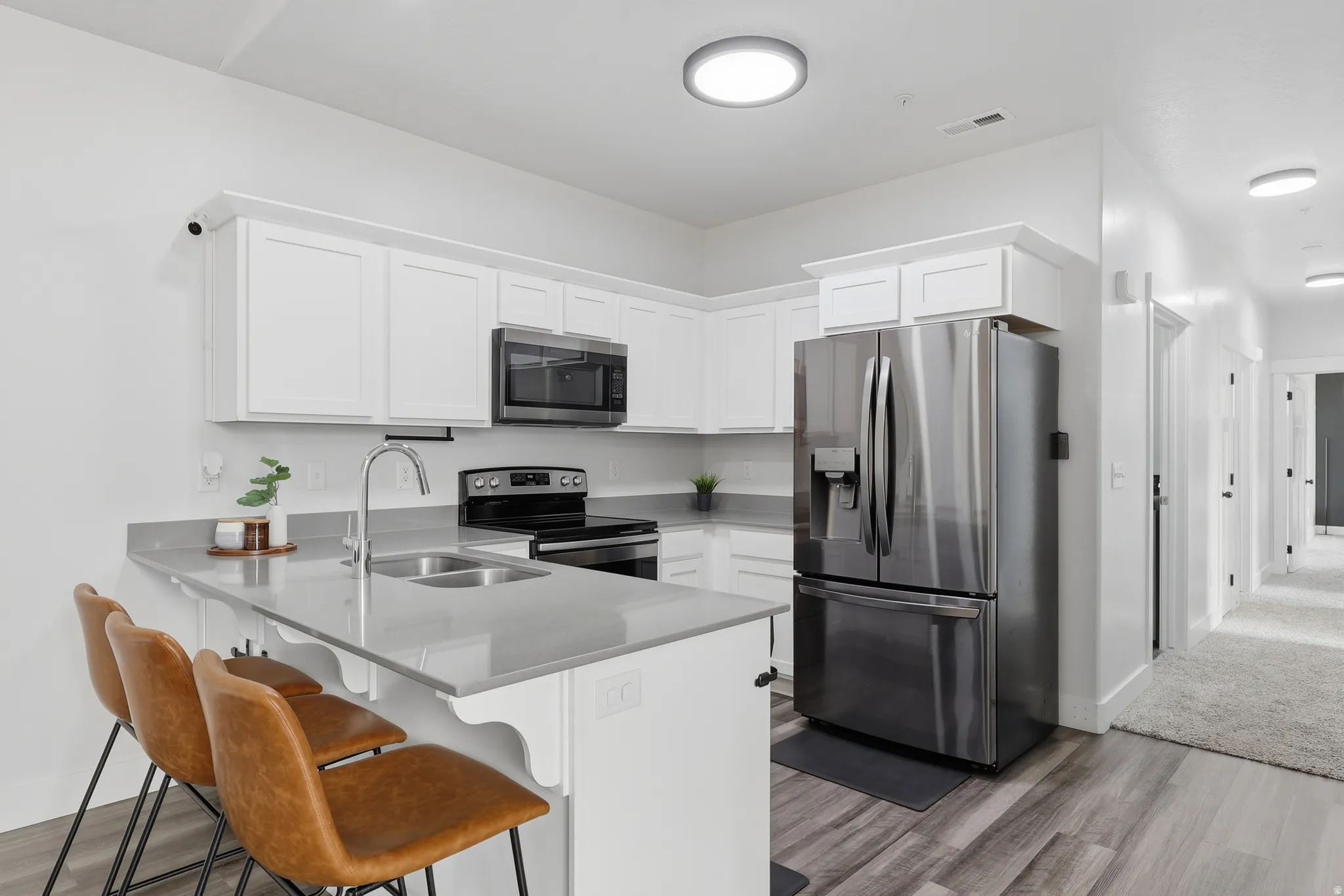 Modern kitchen featuring white shaker cabinetry, stainless steel appliances, light gray countertops, and wood-finish flooring