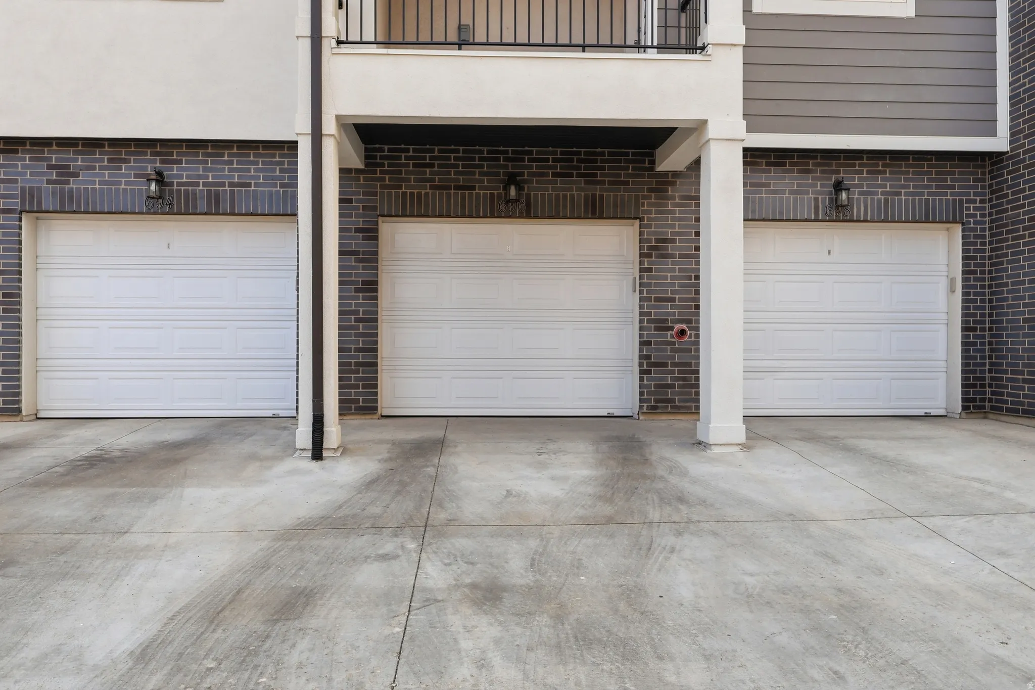 Exterior facade featuring three white panel garage doors, dark brickwork, and concrete driveway