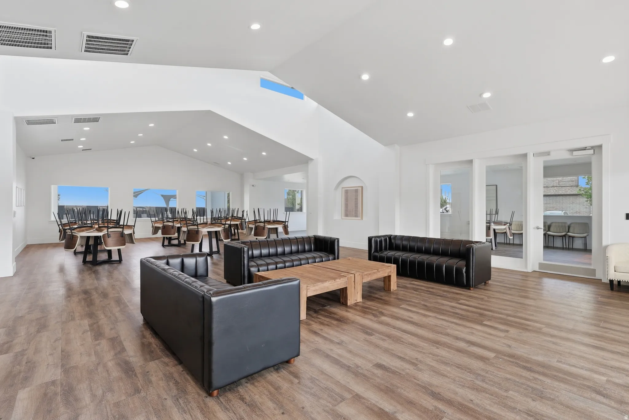 Spacious common area featuring vaulted ceilings, recessed lighting, wood-finish flooring, and large windows