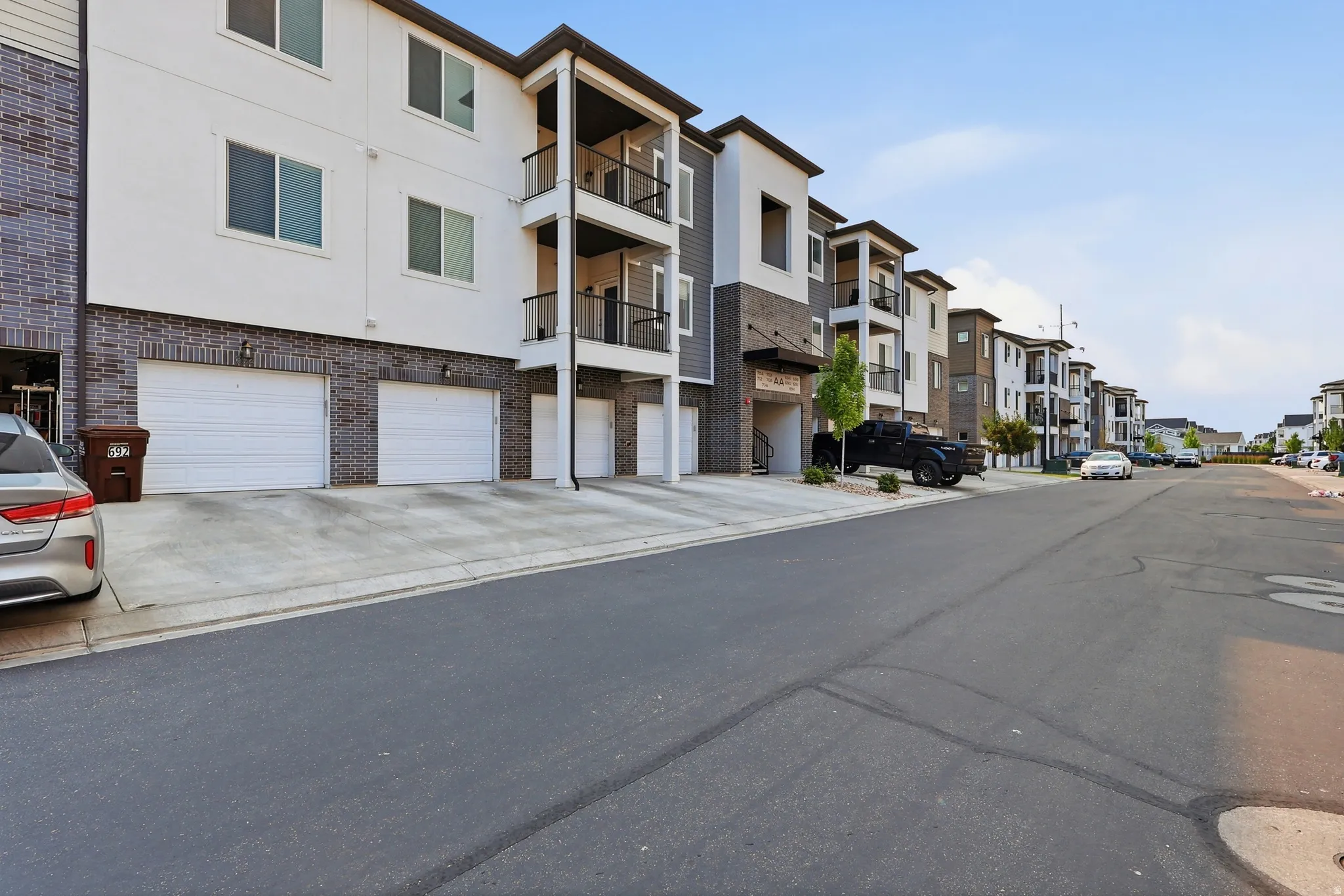 Contemporary multi-level building featuring a brick and siding exterior, multiple private balconies with black railings, individual garage access, and a paved street