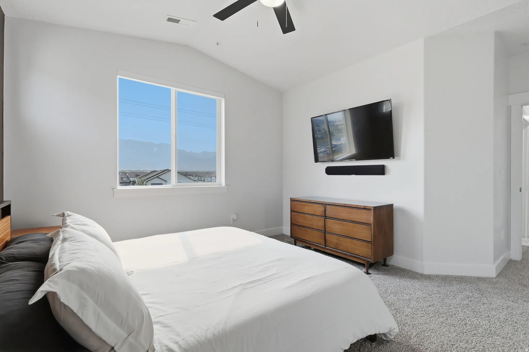Spacious room featuring vaulted ceilings, a large window, light gray carpet flooring, and a modern ceiling fan