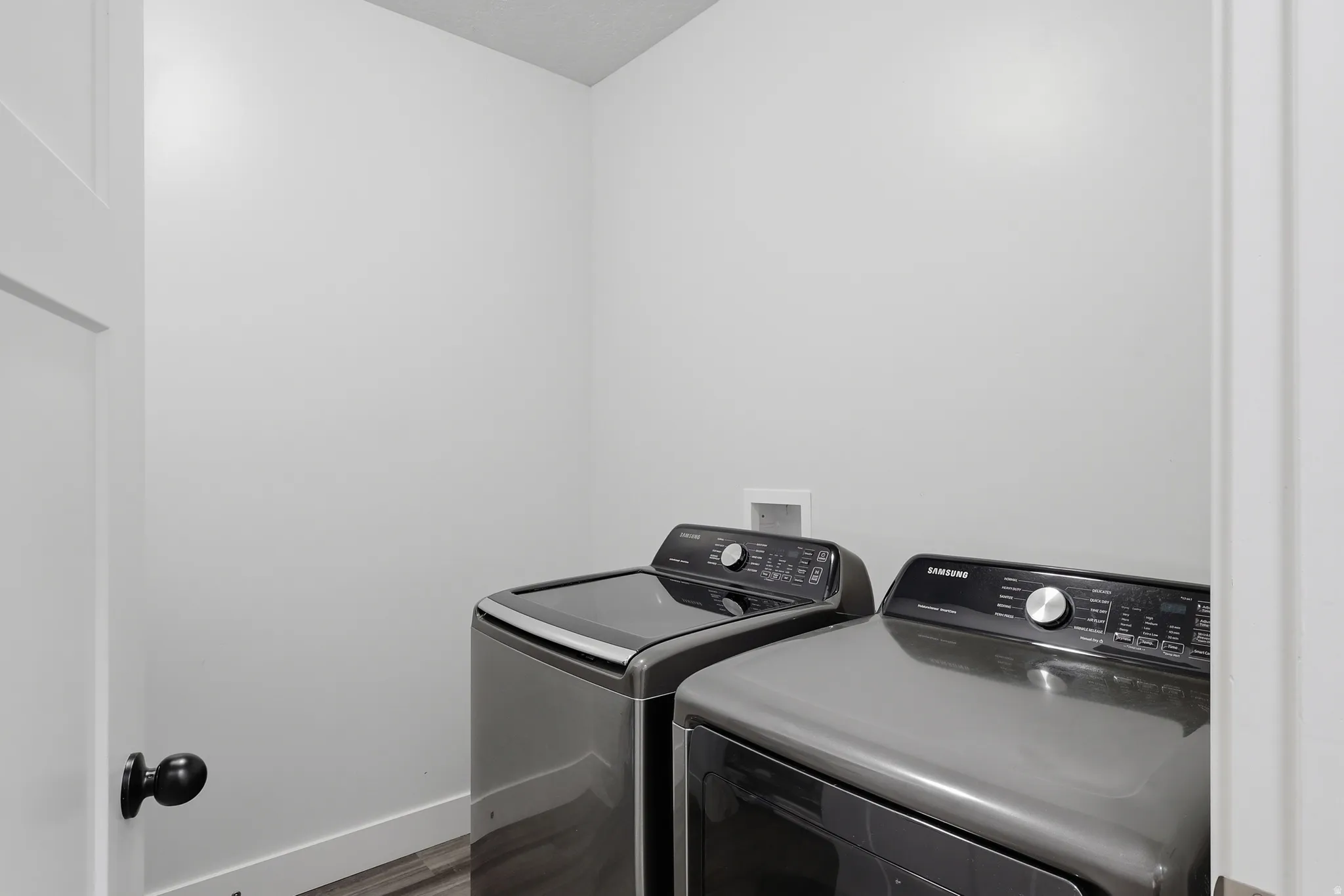 Dedicated laundry space featuring a side-by-side washer and dryer set, white wall paneling, and wood-finish flooring