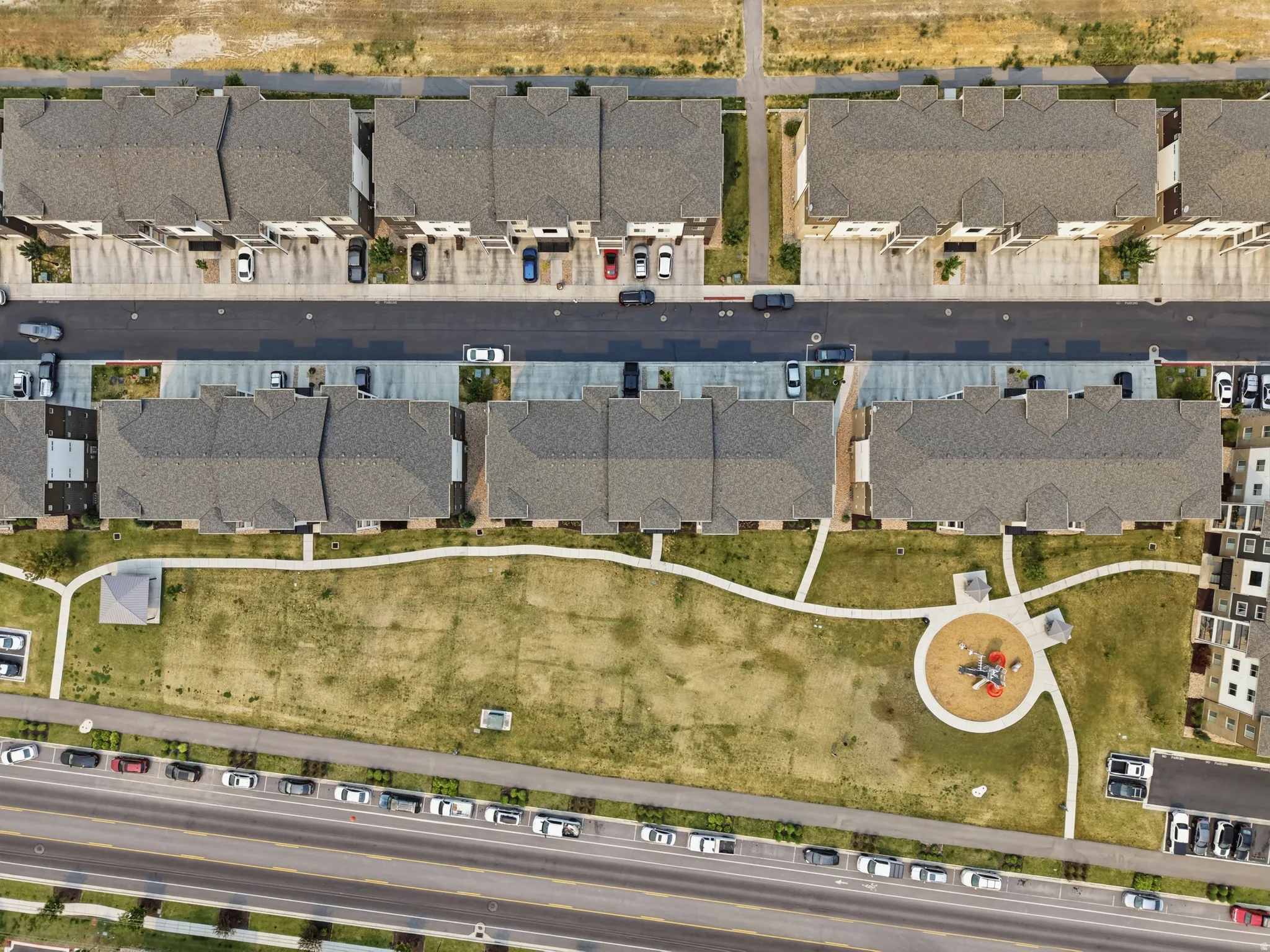 Aerial perspective showcasing a residential development featuring multiple townhome-style buildings with gabled roofs, paved roads, and dedicated parking areas