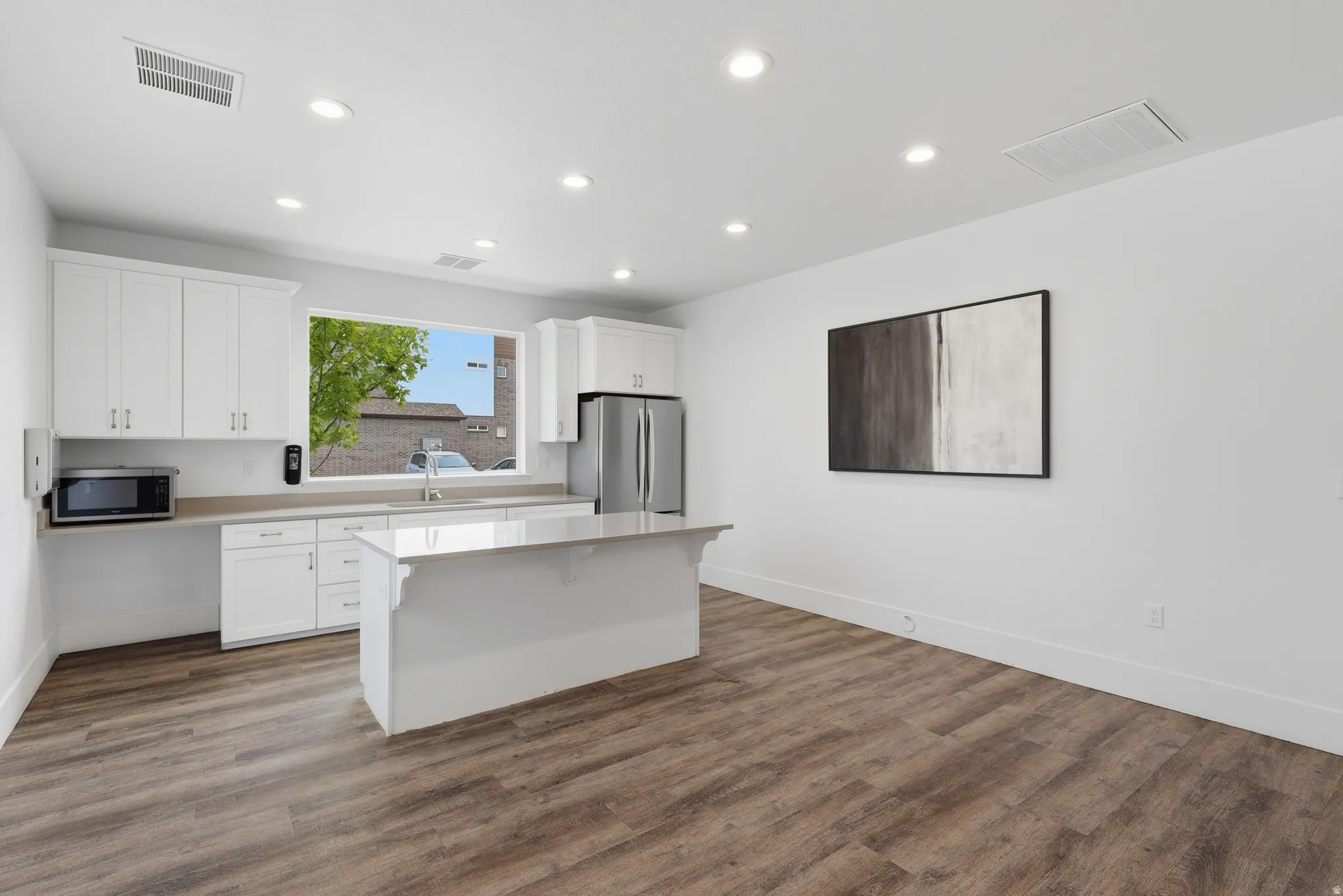 Contemporary kitchen featuring white cabinetry, a central island, stainless steel refrigerator, and wood-finish flooring
