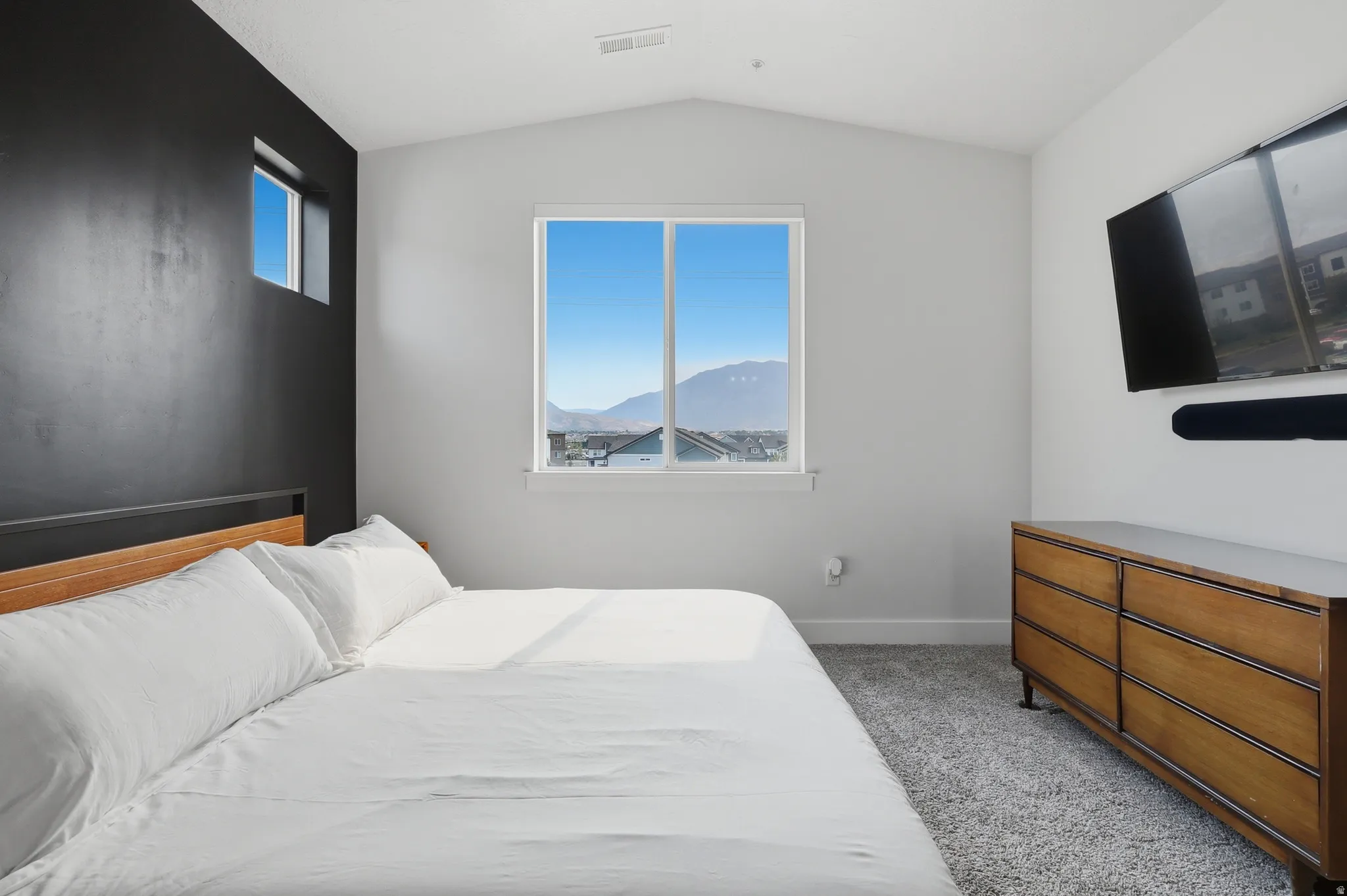 Interior room featuring a large window with mountain scenery, a dark accent wall with a smaller high window, and light gray carpet flooring