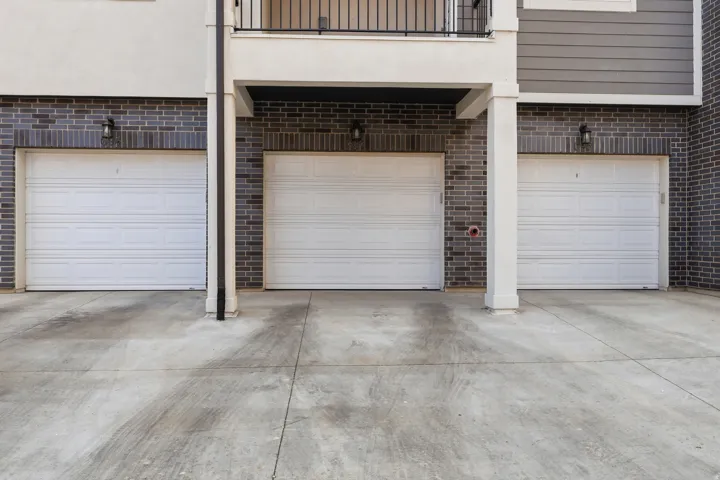 Exterior facade featuring three white panel garage doors, dark brickwork, and concrete driveway