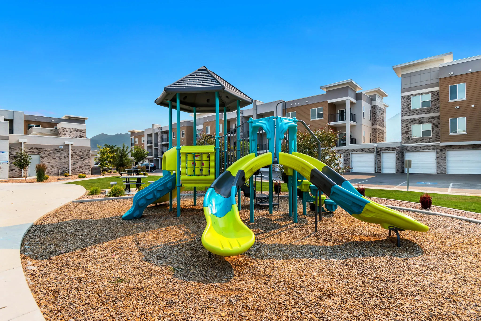 Outdoor playground structure with multiple slides and climbing elements, set on wood chip surfacing