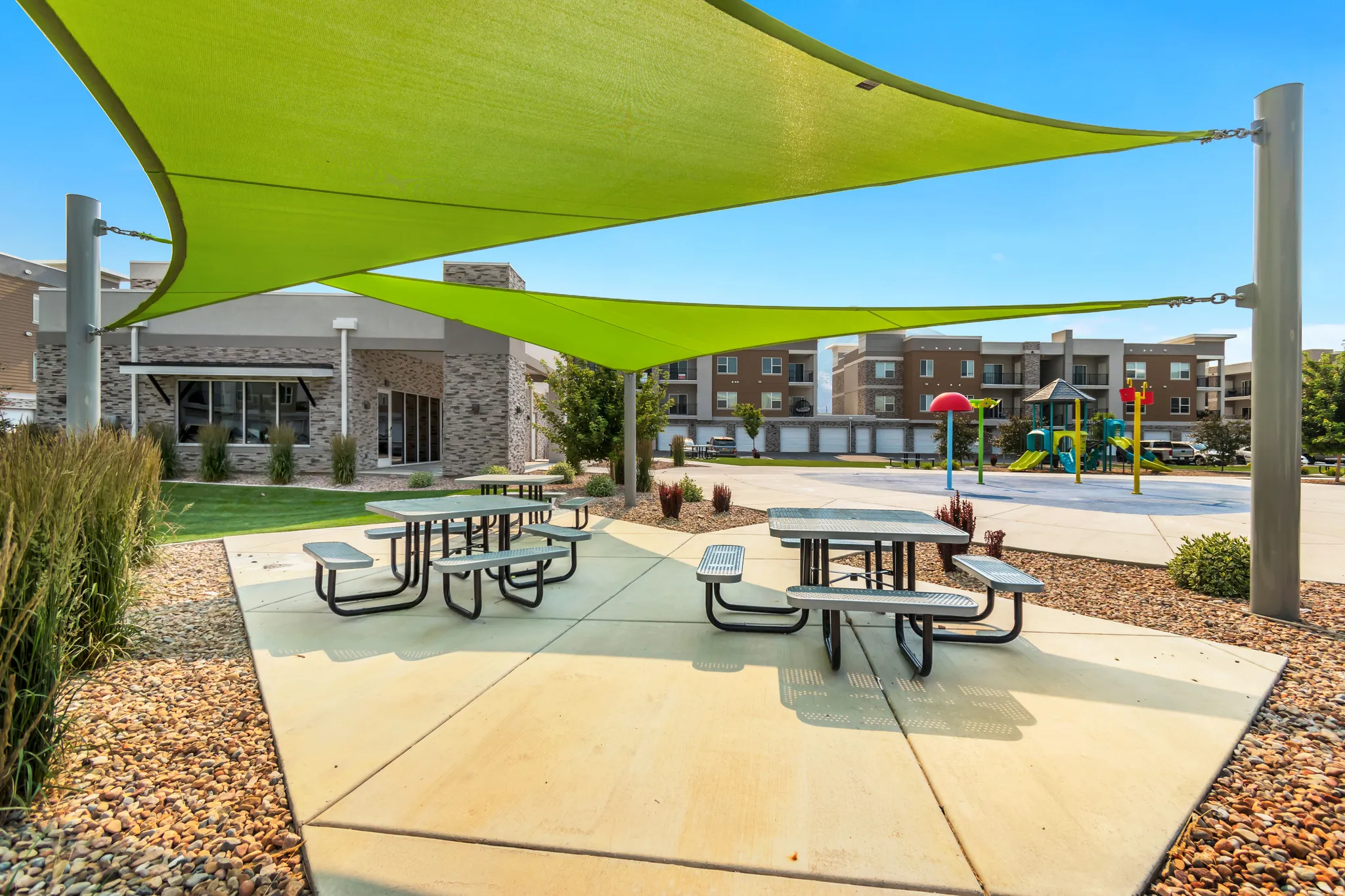Outdoor amenity area featuring two green shade sails, concrete patio, and two picnic tables