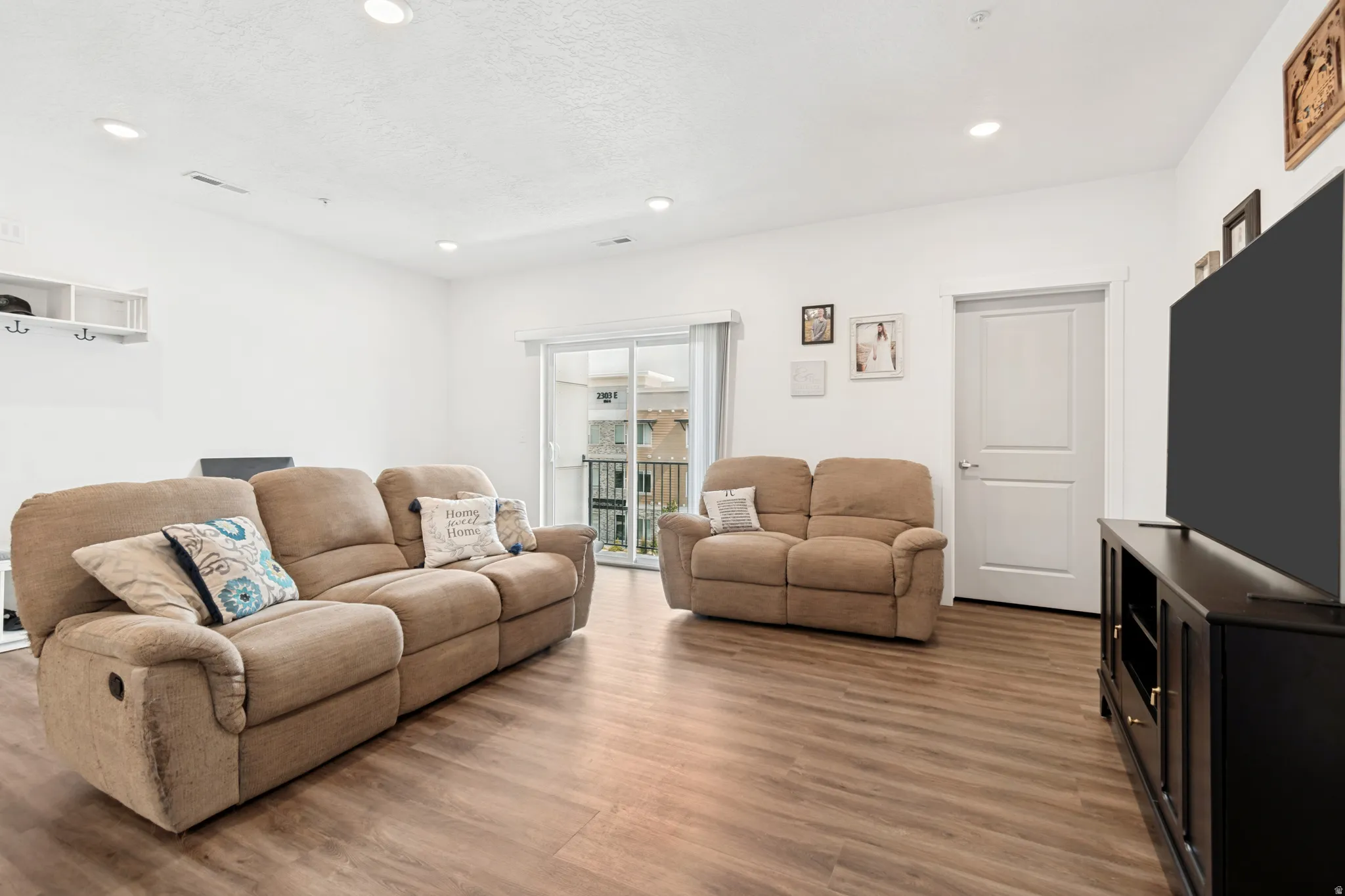 Open living area featuring wood-finish flooring, recessed lighting, white walls, a white two-panel interior door, and sliding glass doors to the exterior