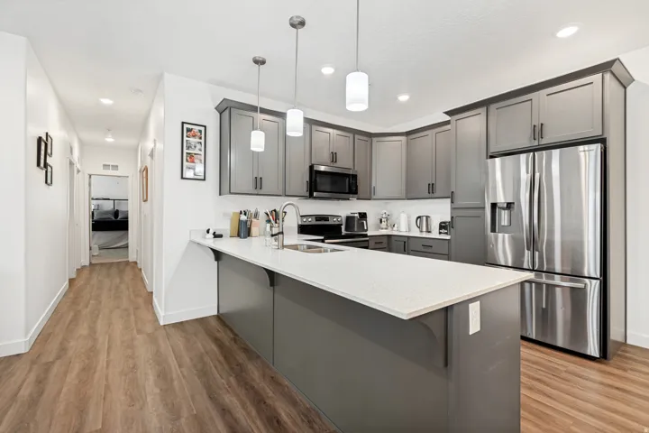 Modern kitchen featuring gray shaker-style cabinetry, a quartz-look island countertop, stainless steel appliances, pendant lighting, and wood-finish flooring