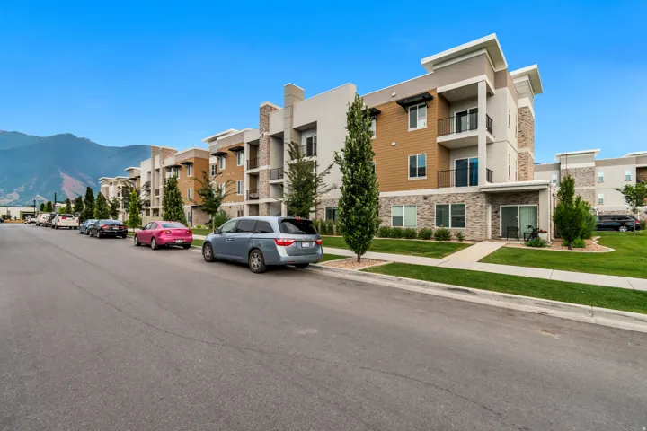 Multi-story residential building featuring balconies with black railings, ground-level patios with sliding glass doors, and a combination of stone veneer and horizontal siding