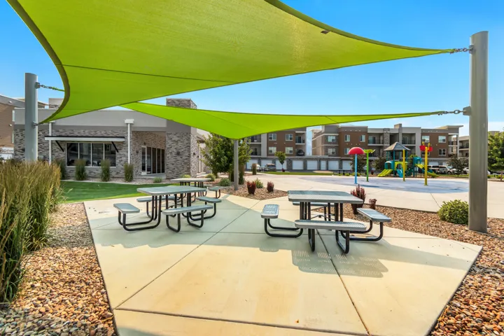 Outdoor amenity area featuring two green shade sails, concrete patio, and two picnic tables