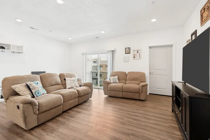 Open living area featuring wood-finish flooring, recessed lighting, white walls, a white two-panel interior door, and sliding glass doors to the exterior