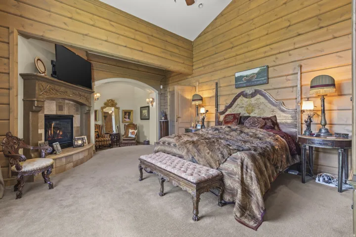 Wood-paneled room featuring a stone-clad fireplace with mantel, an arched entry, and vaulted ceilings