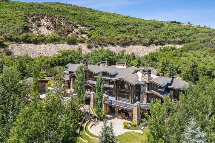 Expansive residence featuring a stone and wood facade, multiple balconies, a terraced lawn, and mature trees