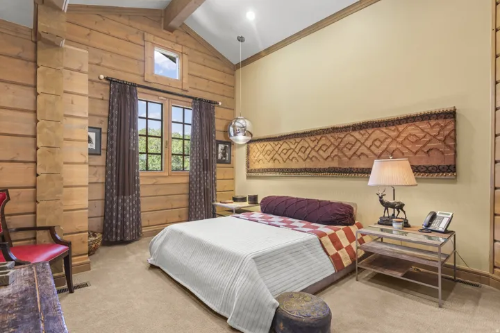 Vaulted ceiling with wood beams, light wood paneling, and a large window with grid panes