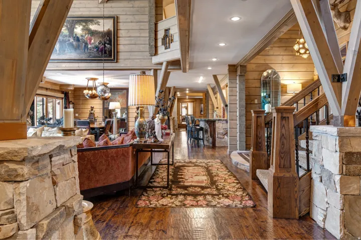 Spacious interior featuring wood-finish flooring, exposed wood beam construction, stone accents, and a built-in staircase with wrought iron balusters