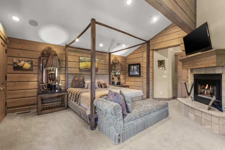 Vaulted ceiling with exposed wood beams, wood-paneled walls, a built-in fireplace with tile surround, a wood mantel, and recessed lighting