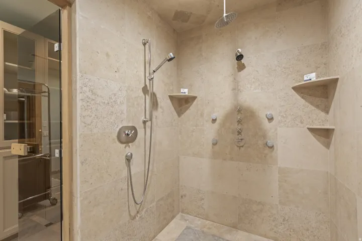 Stone-tiled shower featuring a ceiling-mounted rainfall showerhead, handheld shower fixture, and multiple body jets
