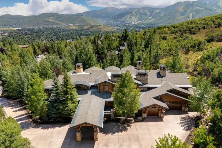 Expansive multi-level property featuring a stone and wood facade, multiple chimneys, an attached two-car garage, a porte-cochère, and a paver driveway