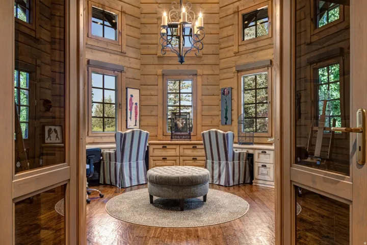 Paneled double doors open to a round room featuring extensive natural wood paneling, multiple windows, built-in cabinetry, and a wrought iron chandelier