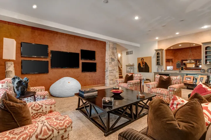 Spacious entertainment area featuring a multi-screen media wall, recessed lighting, and a substantial dark wood-finish coffee table