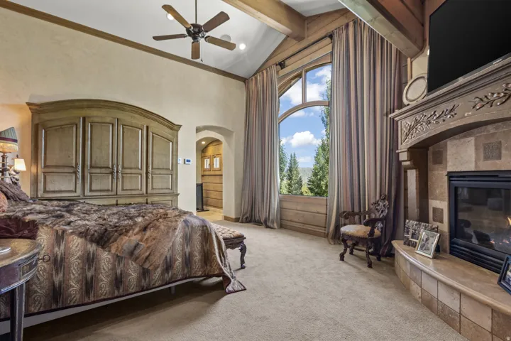 Vaulted ceilings with exposed wood beams, a stone-clad fireplace, and a large arched window