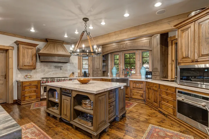 Gourmet kitchen featuring a large central island with light-toned countertop, extensive wood cabinetry, and wood-finish flooring