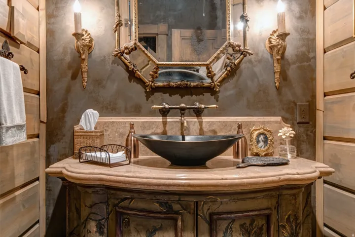Custom vanity with a rounded stone countertop, black vessel sink, and an ornate gold-framed mirror