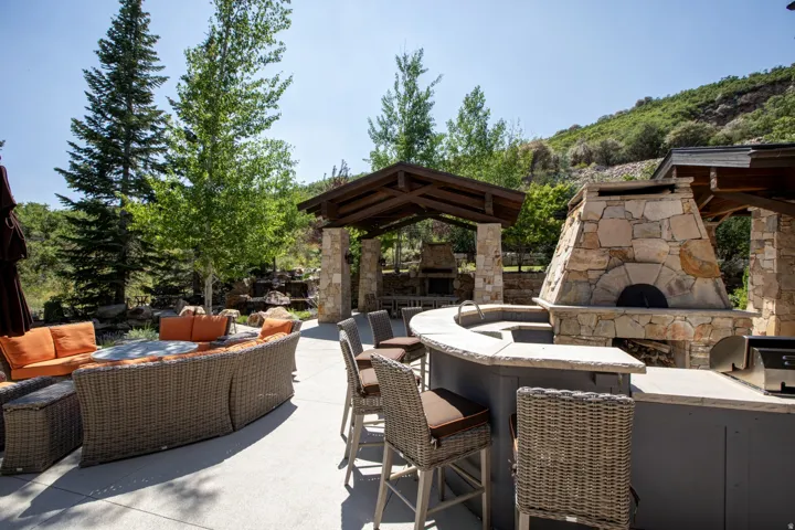 Expansive outdoor entertaining area featuring a stone pizza oven, built-in grill, and curved counter bar with a sink