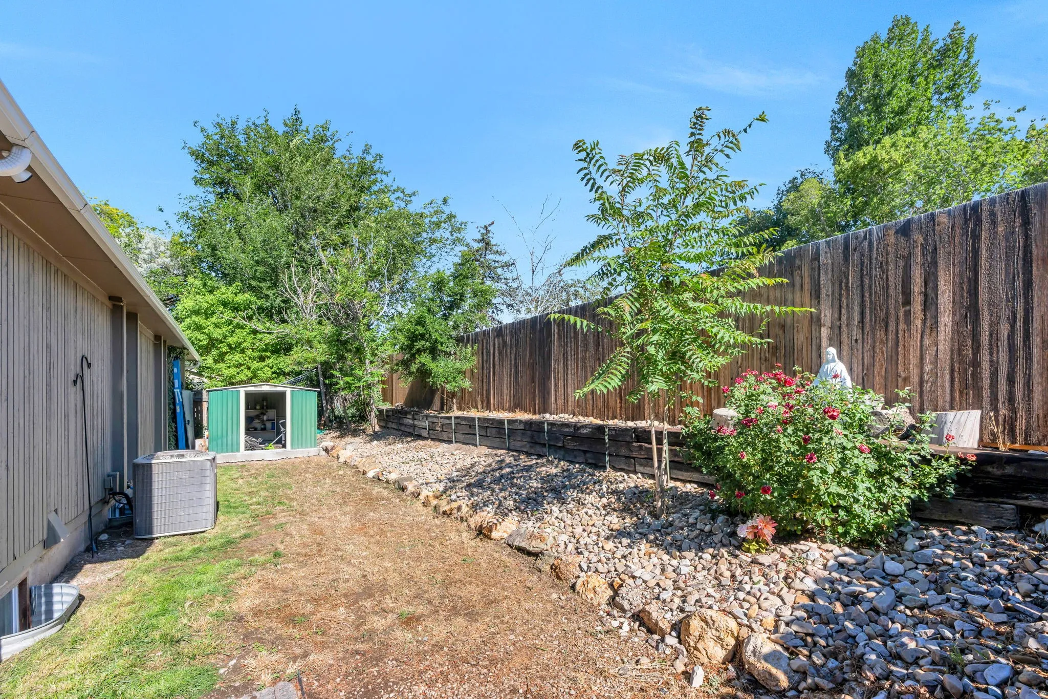 Side yard featuring a gravel and rock landscaping, wood fence, and a storage shed