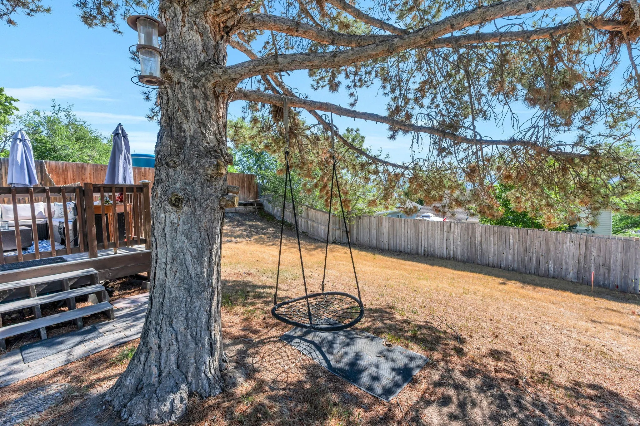 Spacious backyard featuring a large tree, a raised wooden deck with railings, and a privacy fence