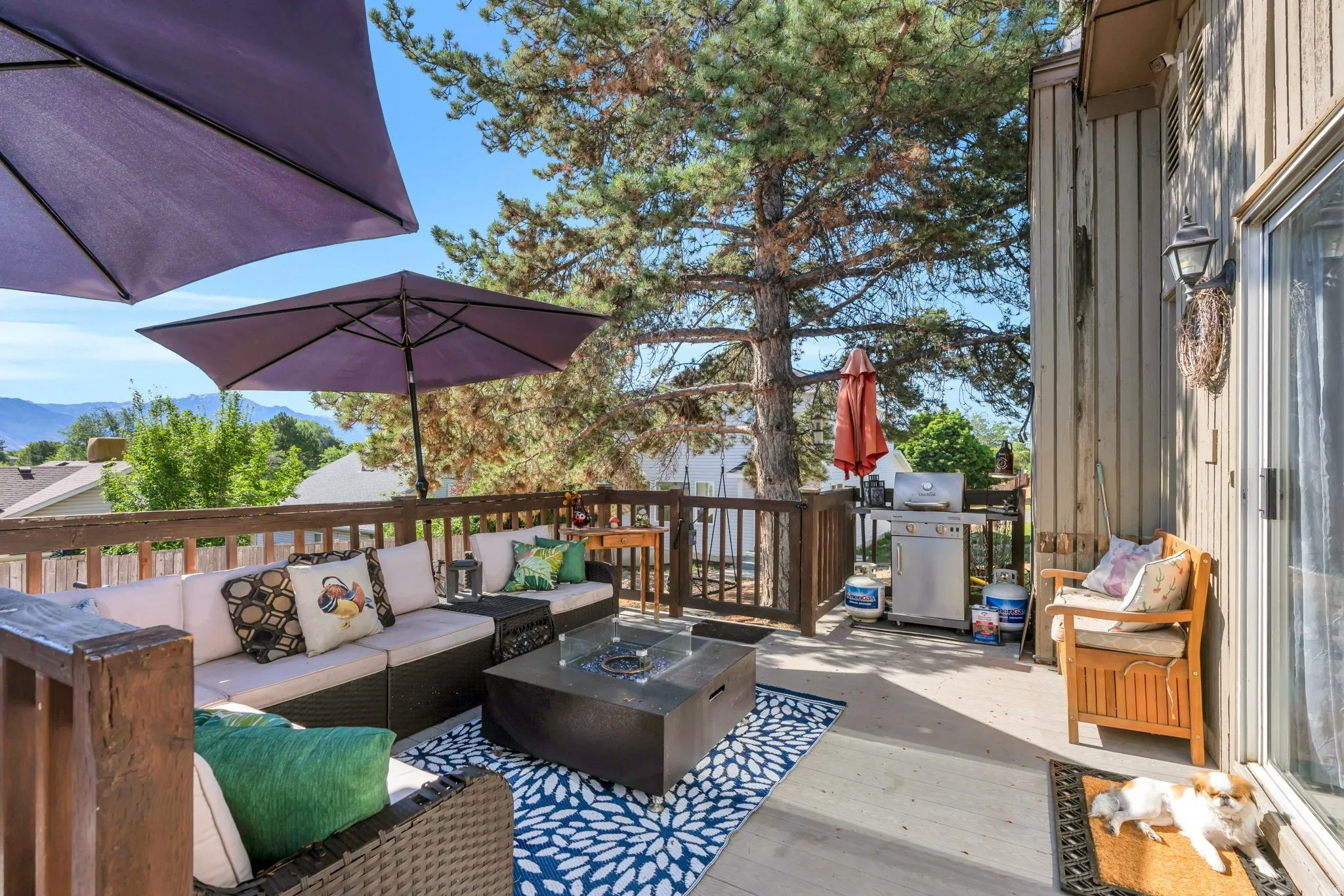 Spacious outdoor deck featuring wood railing, a sliding glass door, and a mature tree providing natural shade