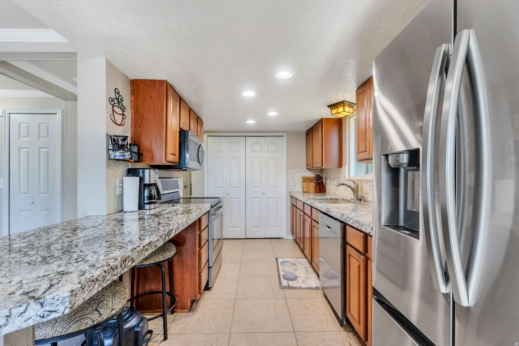 Galley kitchen featuring wood cabinetry, light-toned granite countertops, and stainless steel appliances