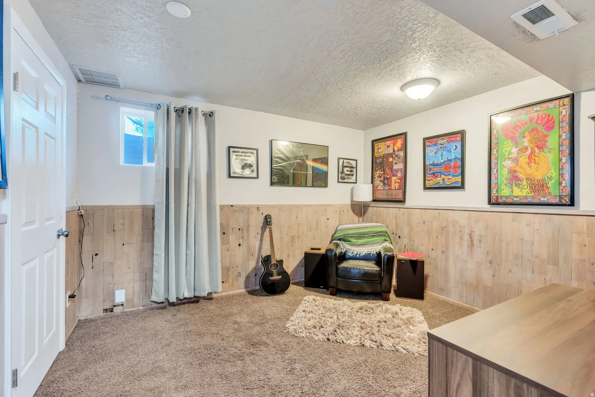 Carpeted room featuring light wood paneling, white walls, and a small window with light-blocking curtains