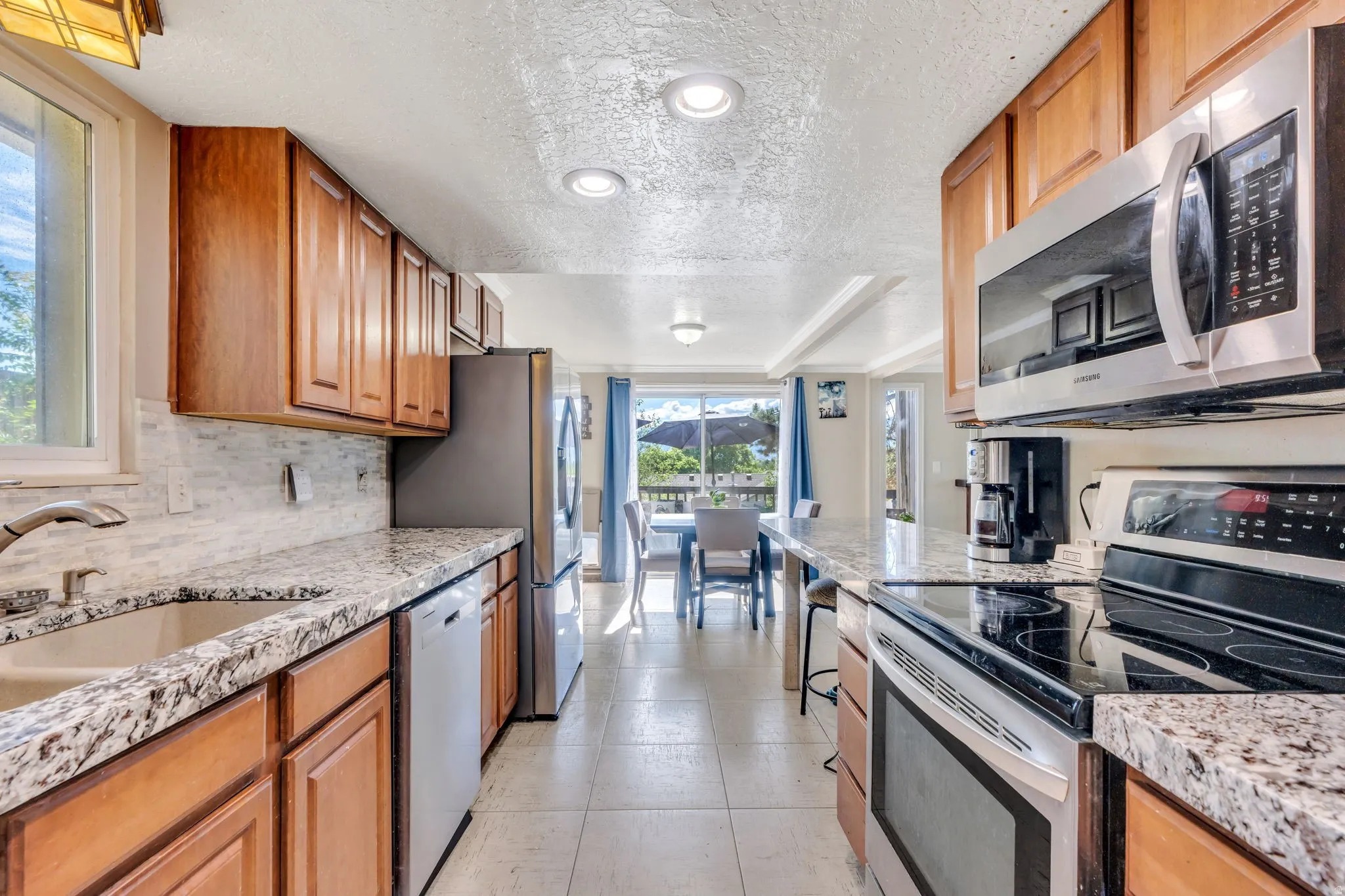 Kitchen featuring wood cabinetry, granite-style countertops, stainless steel appliances, and tile flooring