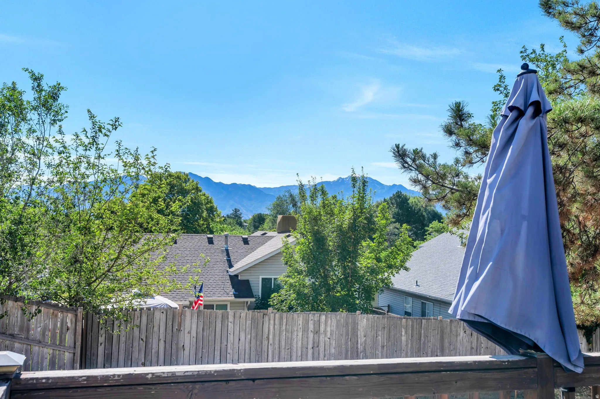 Outdoor deck space with a wooden privacy fence, mature trees, and distant mountain scenery
