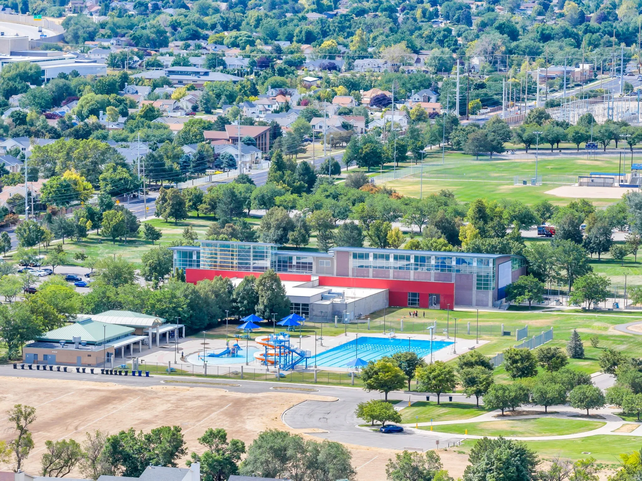 Expansive community recreation center featuring an outdoor swimming pool, water play area, and adjacent sports fields