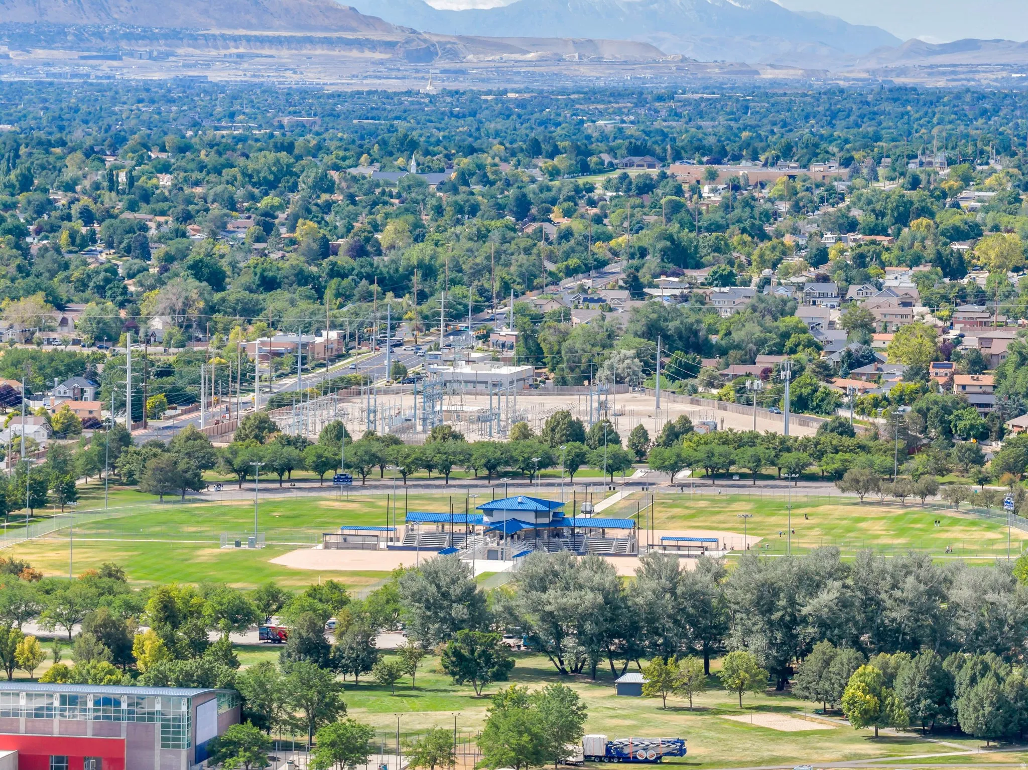 Expansive green space featuring multiple sports fields, mature trees, and a distant mountain range