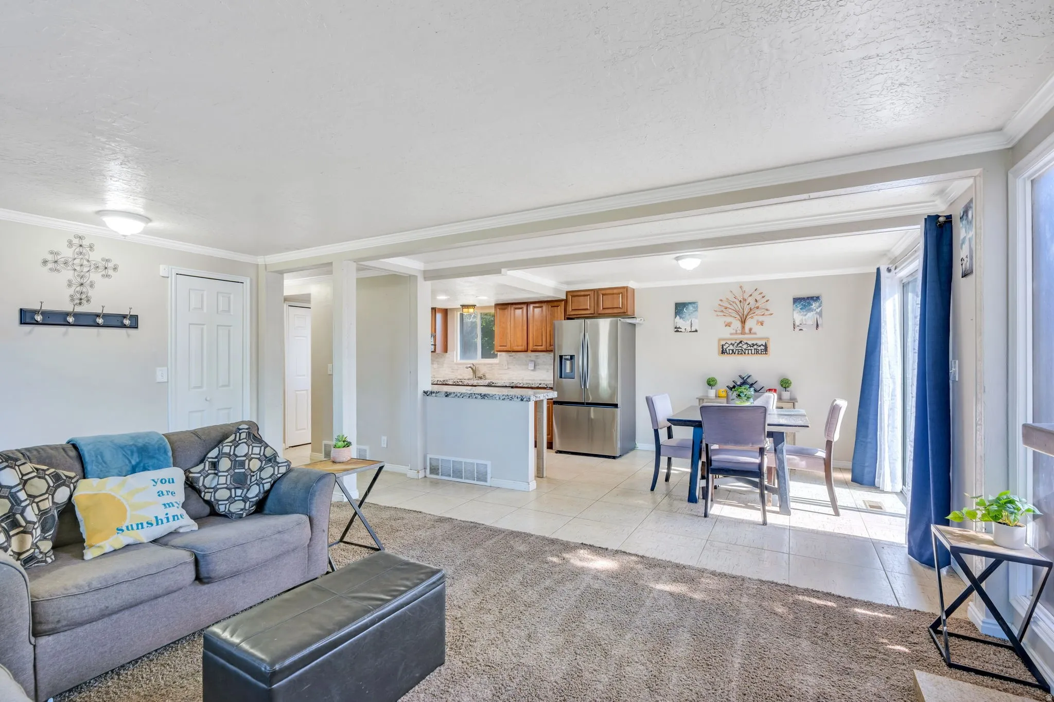 Open-concept living area featuring a carpeted living room, tile flooring, crown molding, and recessed lighting
