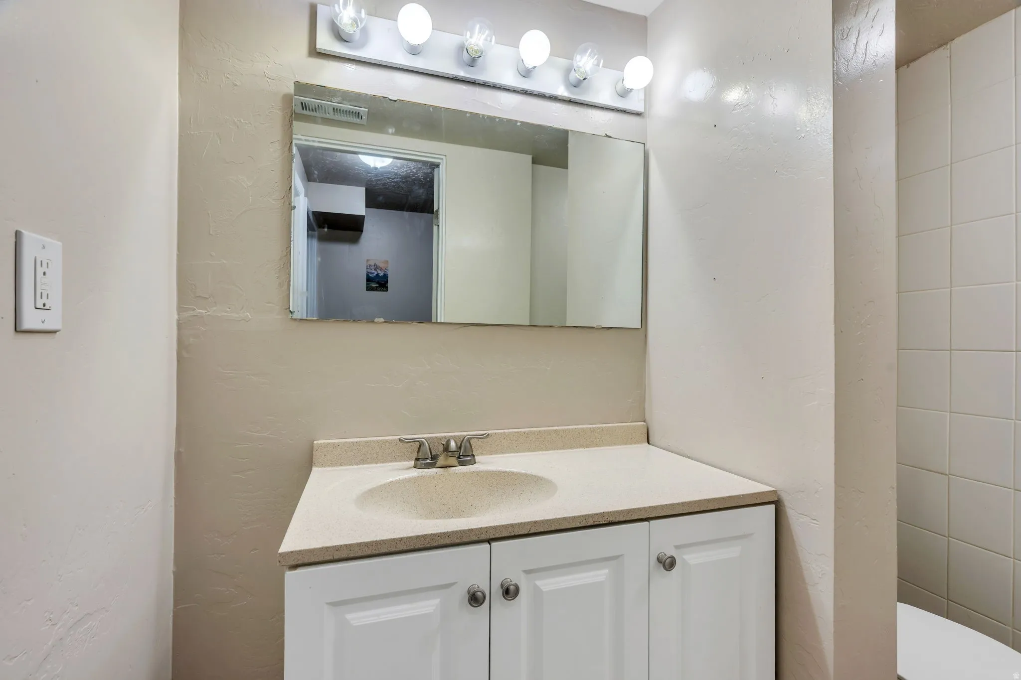 Bathroom vanity featuring a light-colored countertop with an integrated sink, chrome faucet, and white base cabinetry