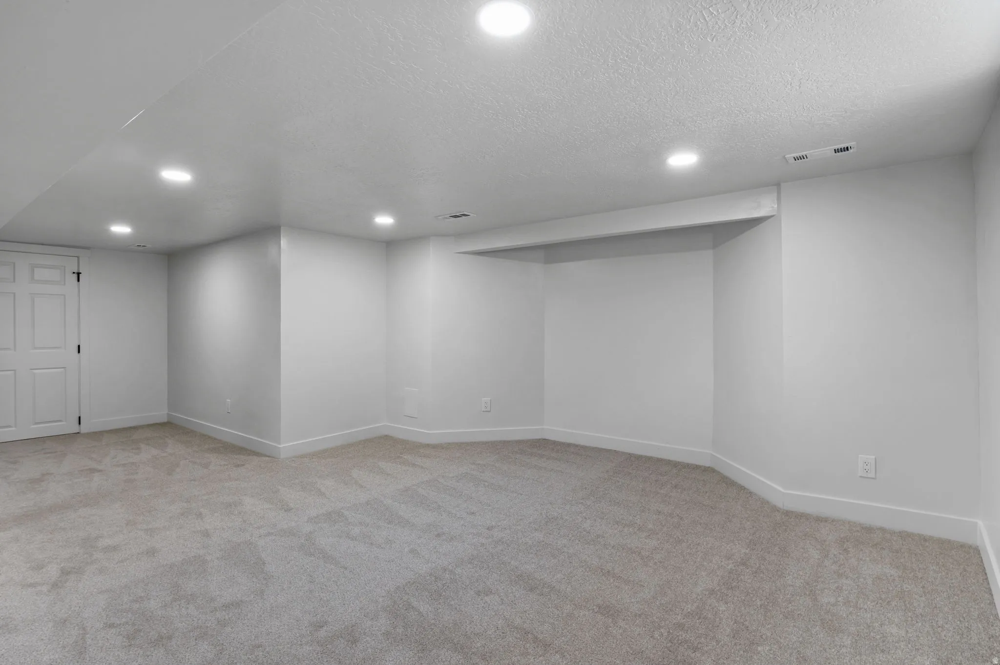 Spacious room featuring light gray carpeting, crisp white walls, recessed ceiling lighting, and a built-in alcove