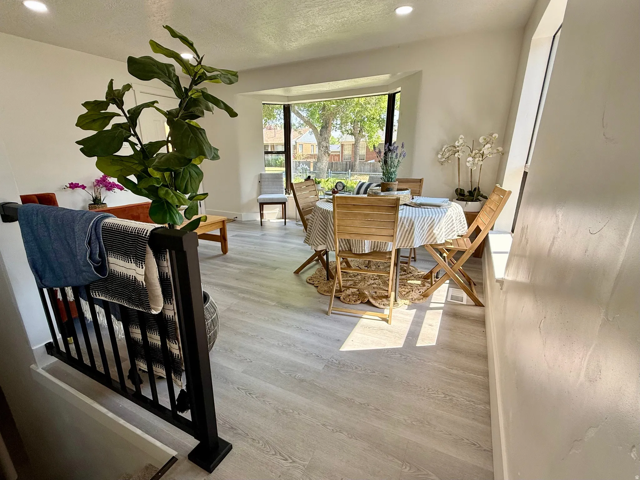 Bright living area featuring light wood-finish flooring, a bay window, recessed lighting, and a black spindle railing